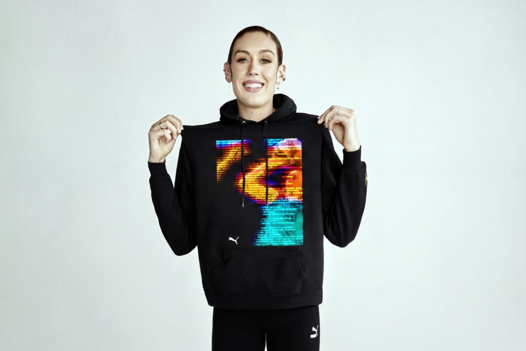 Person smiling while holding up a black hoodie with a colorful graphic on the chest